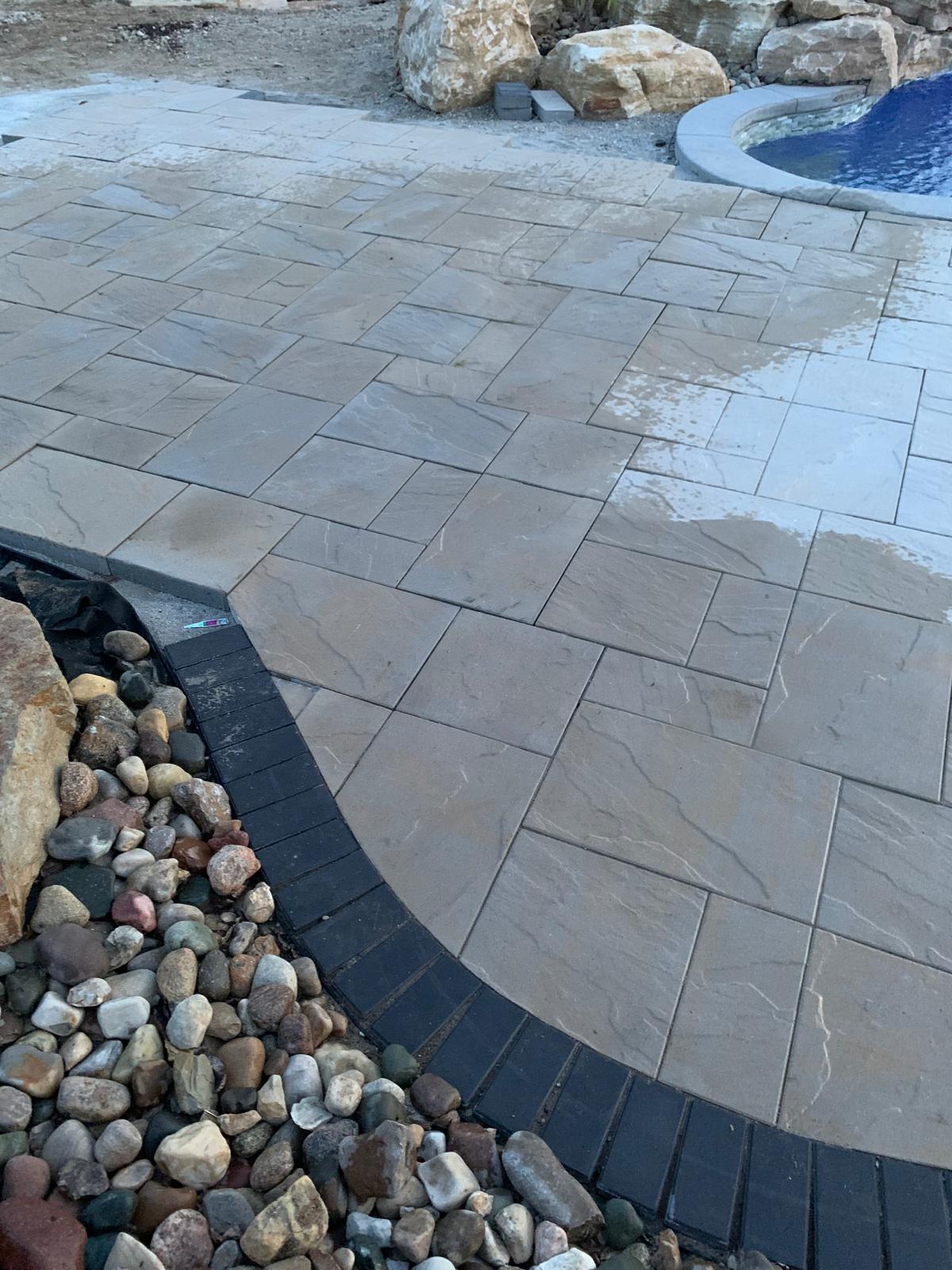 Finished flagstone patio with dark paver border and river rock bed